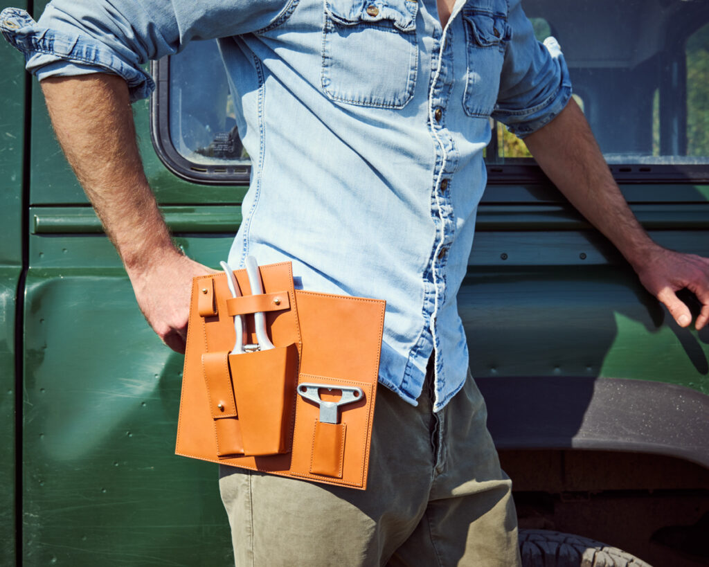 L'Atelier du Vin x Felco leather case hanging from the model's belt with a 4x4 in the background