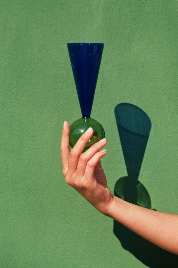 la flûte à champagne se métamorphose : la silhouette traditionnelle en forme de tulipe laisse place à une forme plus directe et moderne, un cône minimaliste et élancé. Le pied plat traditionnel se transforme en une sphère captivante, évoquant une bulle de champagne, réalisée en verre transparent et délicatement coloré.